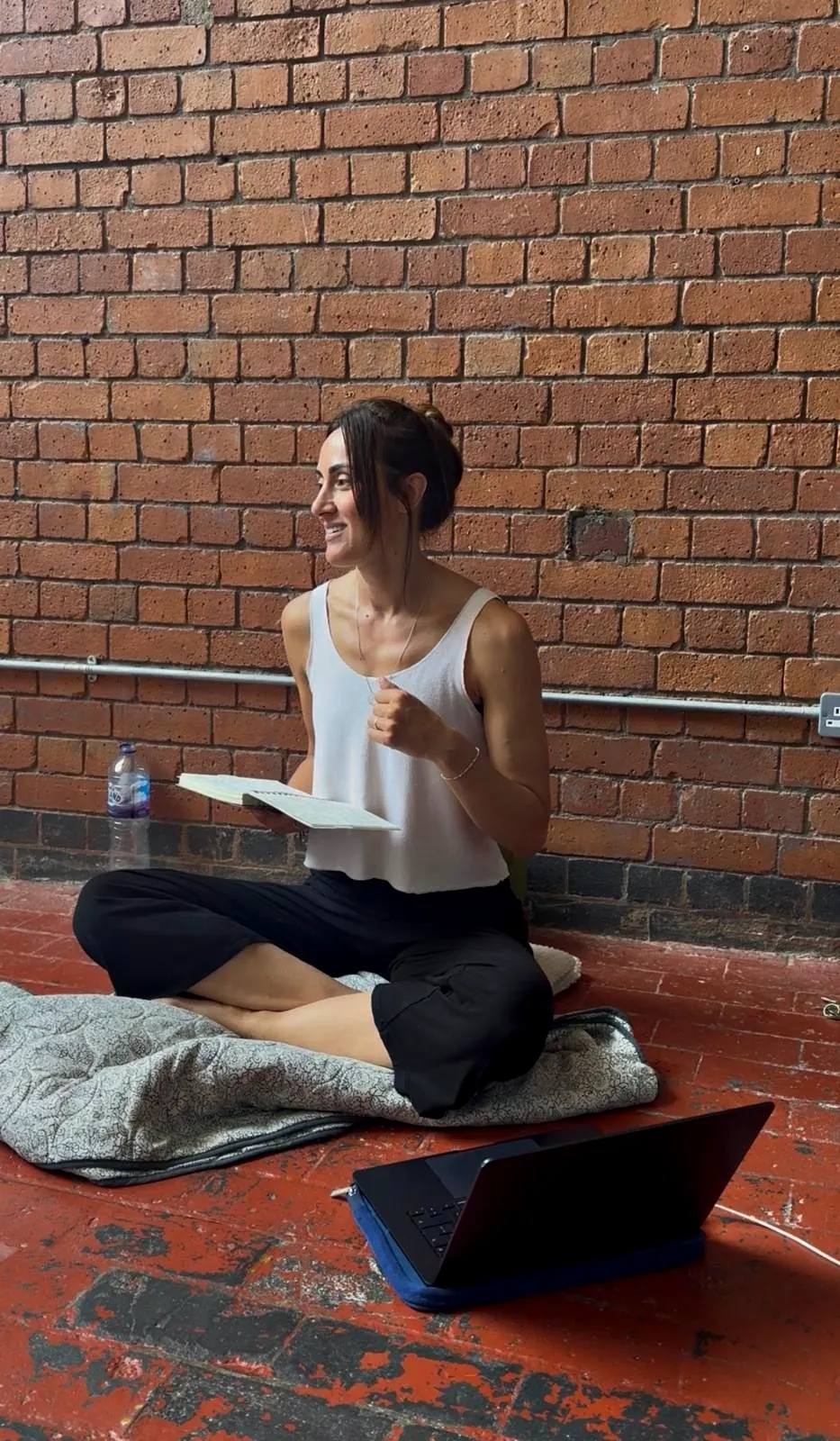 Liane sitting cross legged against a brick wall with her notebook, laughing