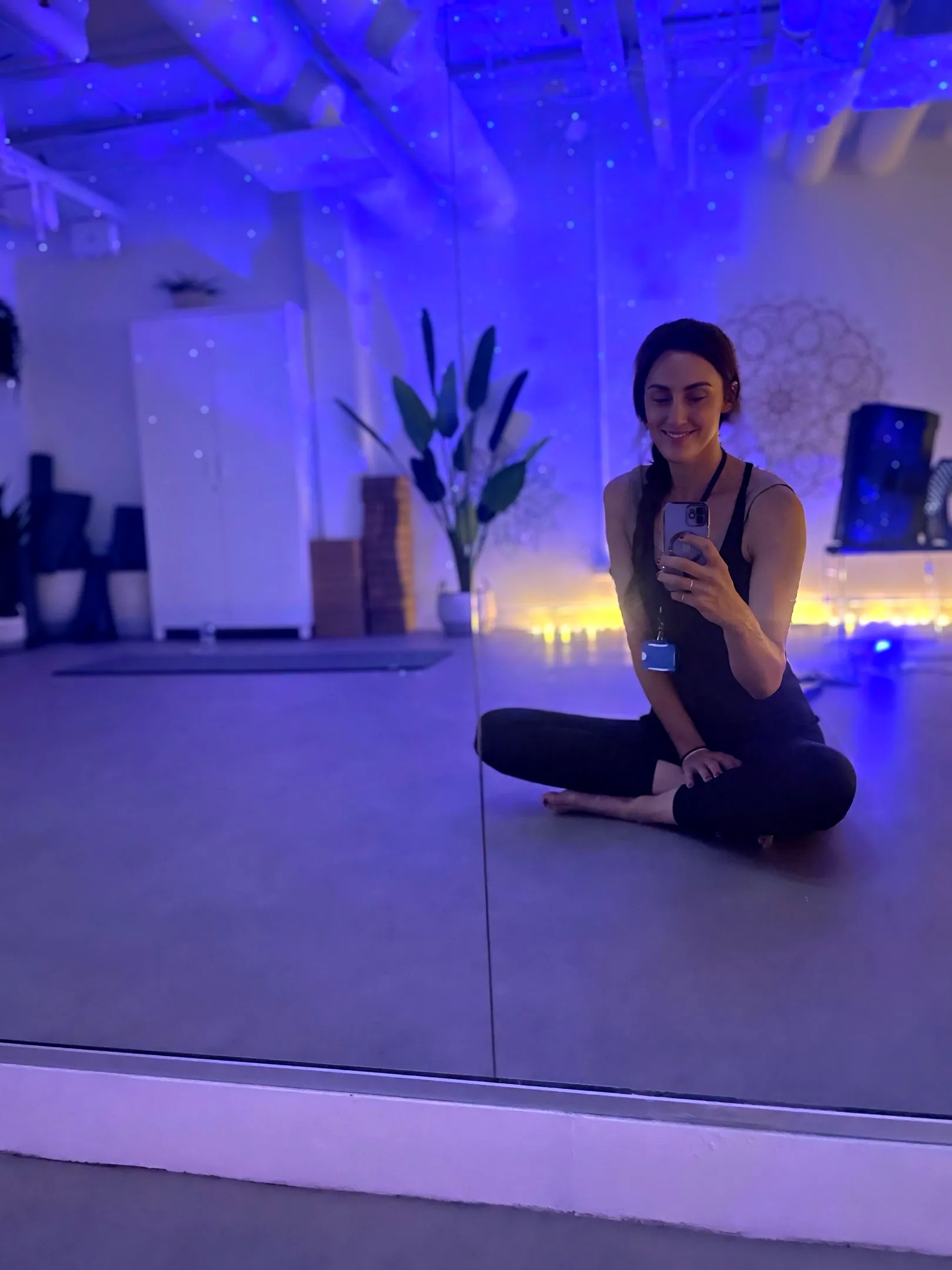 Liane sitting cross legged in the mirrored studio under purple light