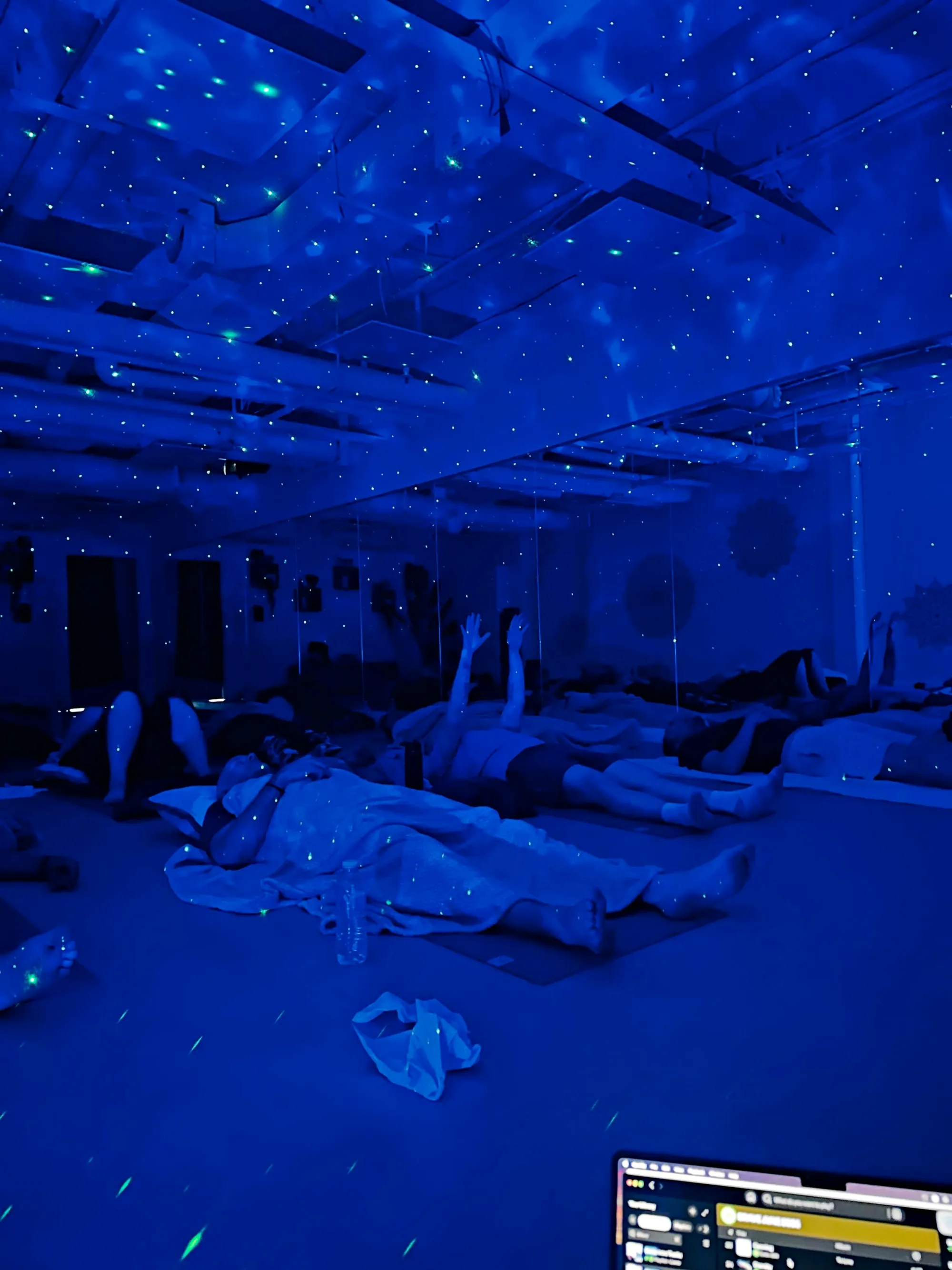 A group breathwork session under blue light, everyone lying on mats under blankets