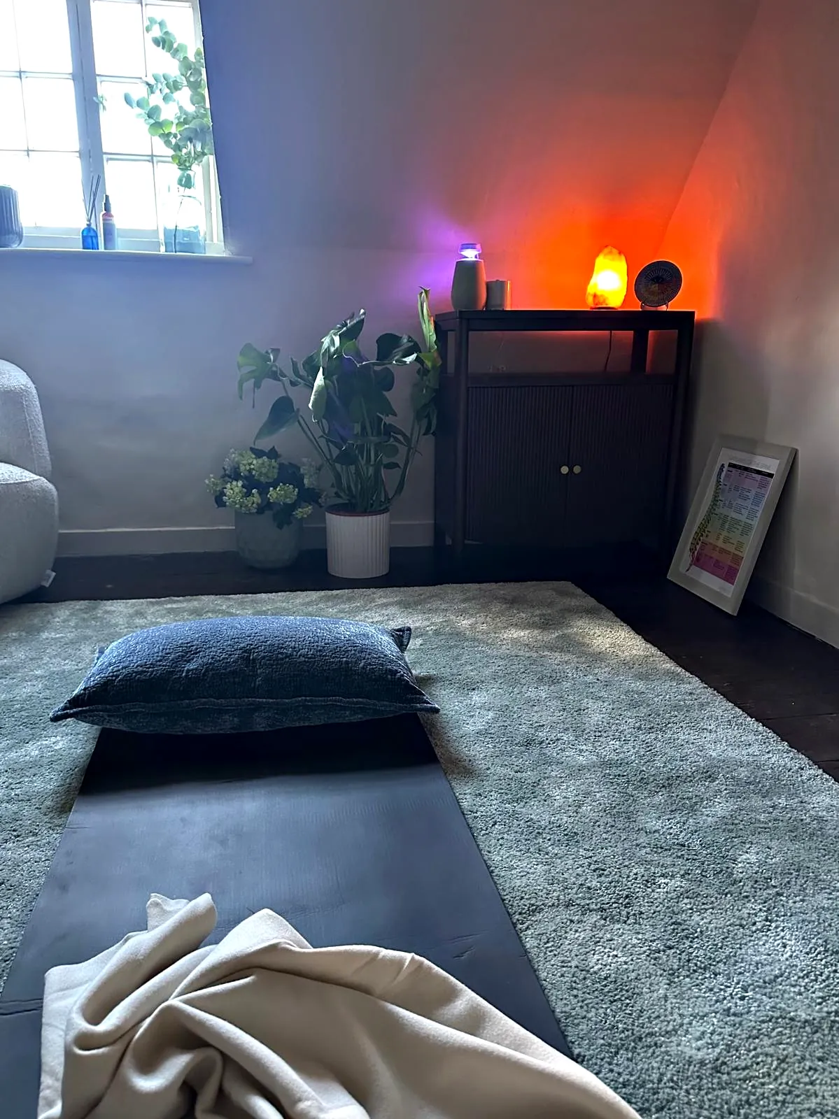 A mat, cushion and blanket laid out on the rug at The Brave Studio, the lamps lit