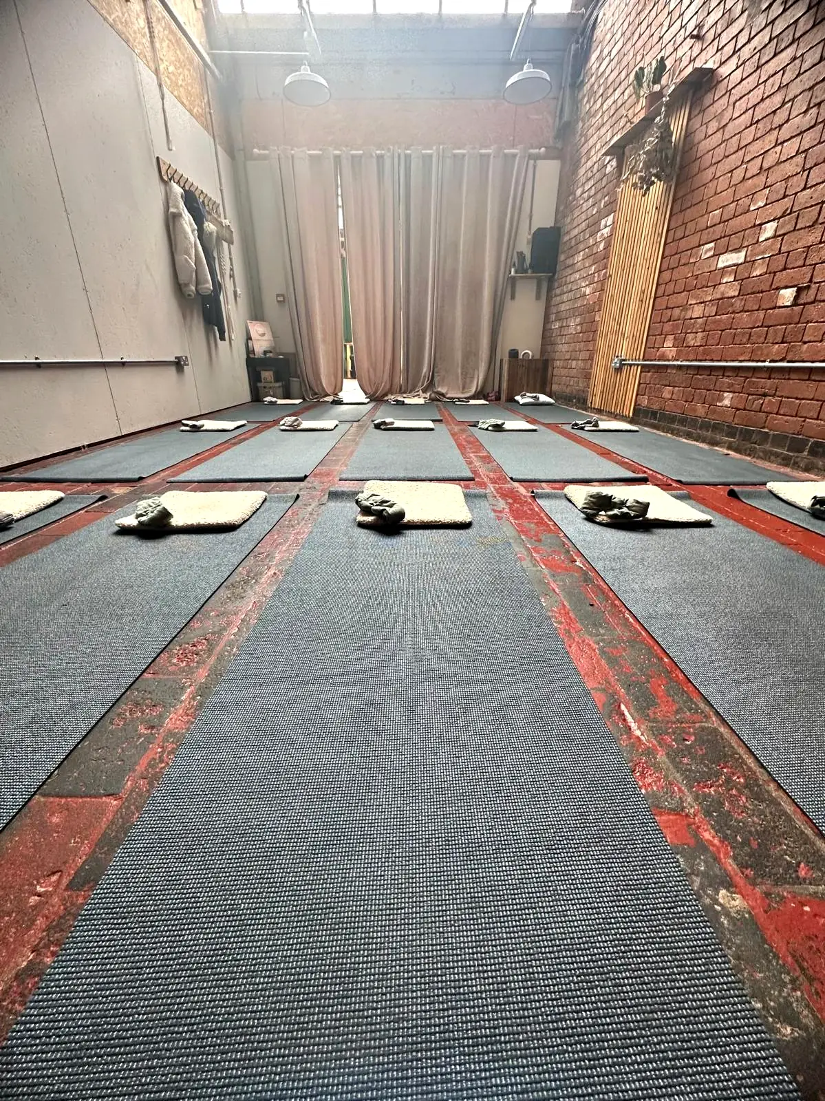 A long room set out for a group session, mats, pillows and eye masks in rows