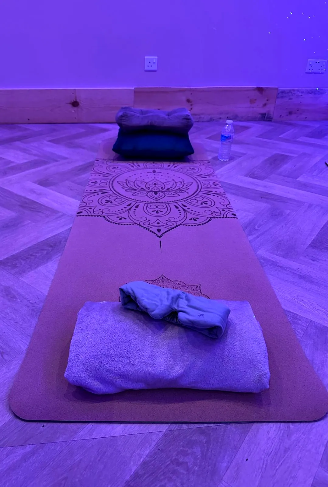 A mat with a cushion and a folded blanket under purple light